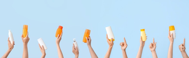Many hands with bottles of sunscreen cream on light blue background