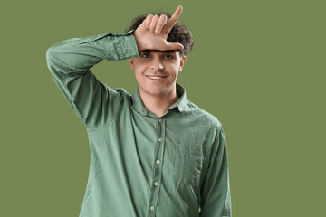 Young man showing loser gesture on green background