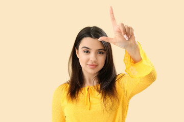 Young woman showing loser gesture on beige background