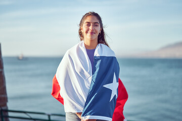 smiling chilean woman holding over the shoulders a flag of Chile outdoors against blue sky and...