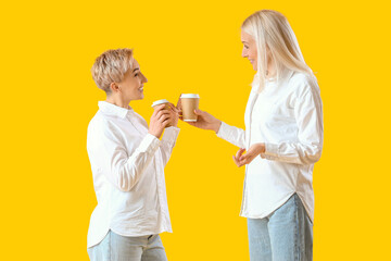 Beautiful mature women with coffee on yellow background