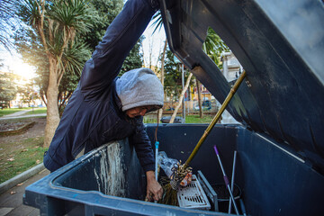 Homeless man looking into trash box in search for food on church background. Homelessness problem concept