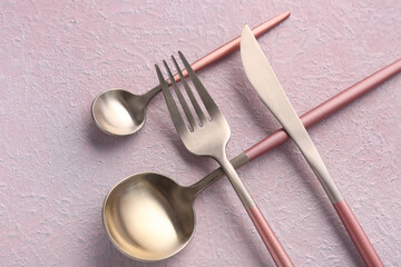 Stainless steel cutlery with pink handles on lilac background