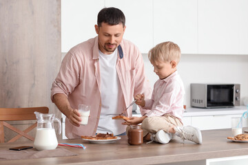 Little boy with his father eating chocolate paste toasts and drinking milk in kitchen