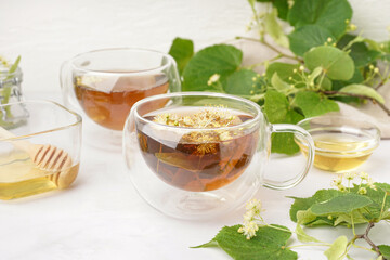 Glass cups of linden tea and bowls with honey on white background