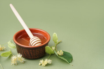 Bowl with linden honey and dipper on green background