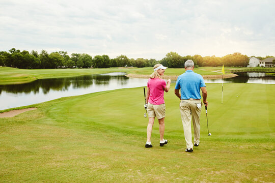 Mature couple, club and walking for golf game outdoor, talking and sports support of recreation practice. Woman, man and love for hobby lesson, advice or discussion of retirement activity in nature