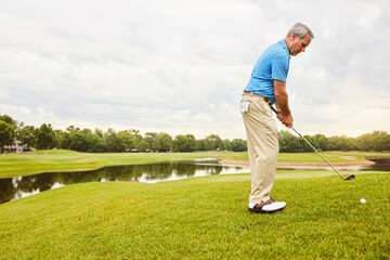 Obraz premium Mature, man and swing on grass for golf or ball to improve balance with coordination and retirement leisure. Golfer, club and play on field for physical activity, mobility and outdoor sport.