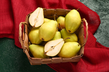 Wicker basket with fresh pears on green background