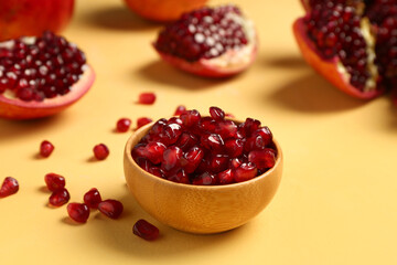 Fresh pomegranates and bowl with seeds on yellow background
