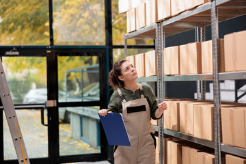 Employee managing products supply in logistics department warehouse, controlling goods distribution before preparing customers orders. Storehouse supervisor standing near shelves with cardboard boxes