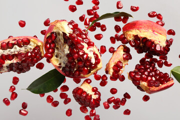 Flying fresh pomegranates with seeds and leaves on grey background
