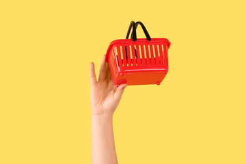 Woman holding mini shopping basket on yellow background