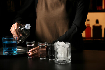 Female bartender with shots of cold vodka on table in bar