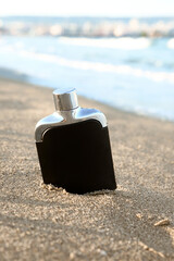 Black perfume bottle on beach sand near ocean