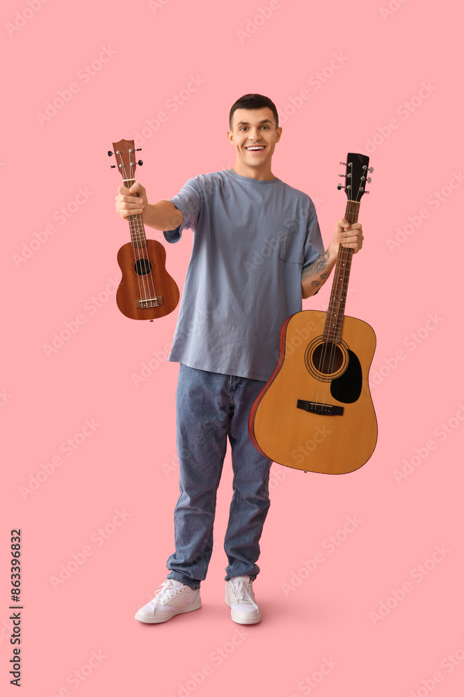 Wall mural Handsome young man with guitars on pink background