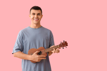 Handsome young man playing ukulele on pink background
