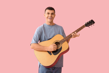 Handsome young man playing guitar on pink background