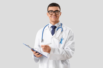 Male urologist with blue ribbon writing in clipboard on light background. Prostate cancer awareness concept