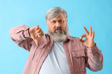 Displeased mature bearded man showing OK and thumb-down gestures on blue background