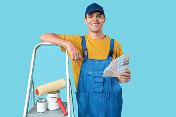 Young painter with color palettes and ladder on blue background