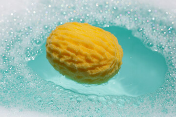 Yellow bath sponge floating on blue water with soap foam