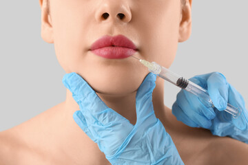 Young woman receiving filler injection in face on grey background