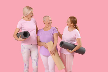 Mature women with yoga mats on pink background
