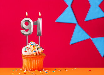 Birthday cupcake with candle number 91 on a red background with blue pennants
