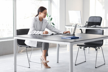 Young Asian businesswoman working with laptop and notebook at table in office
