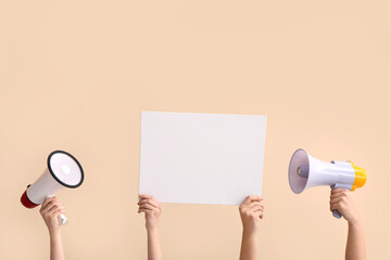 Female hands with megaphones and blank poster on beige background