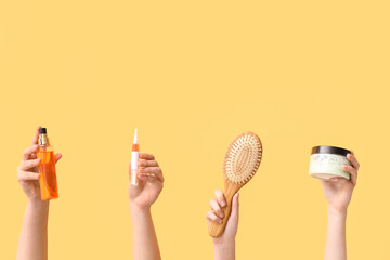 Female hands with different cosmetic products and hair brush on yellow background