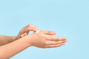 Woman applying cosmetic cream on blue background