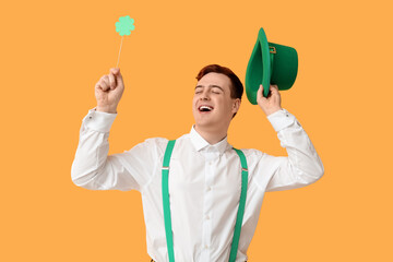 Happy young man with leprechaun's hat and clover on yellow background. St. Patrick's Day celebration
