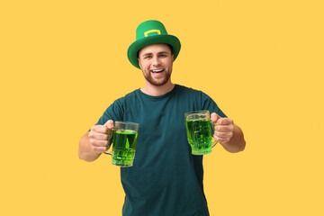 Handsome young man in leprechaun's hat with mugs of beer on yellow background. St. Patrick's Day celebration