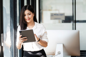 Asian professional business woman looking at online trade app. Beautiful businesswoman CEO holding digital tablet  standing at workplace in office.