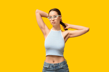 Beautiful young woman with piercing navel on yellow background