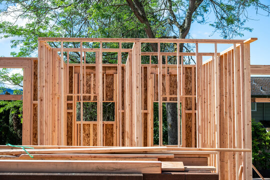 New home construction in residential neighborhood, first floor of structural framing in progress on a sunny summer day
