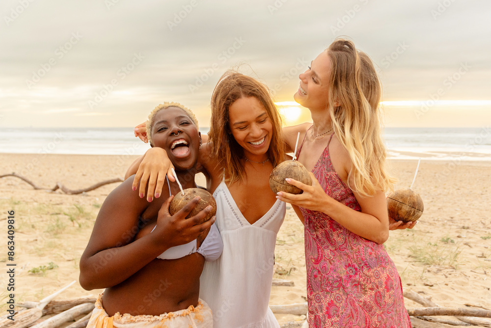 Wall mural group of three female friends hugging and having a good time while enjoying a drink served in a coco