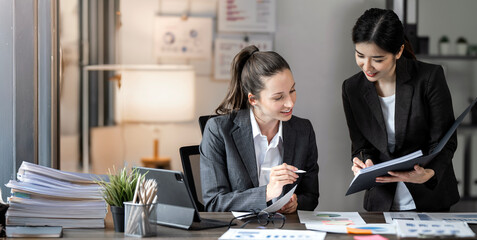 Two businesswoman pointing to graphs and charts to analyze market data,  net profit to plan new sales strategy to increase production capacity.