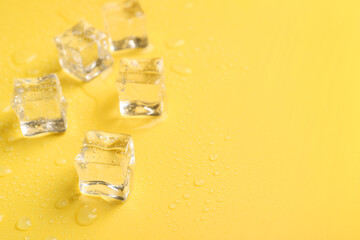 Crystal clear ice cubes on yellow background, closeup. Space for text