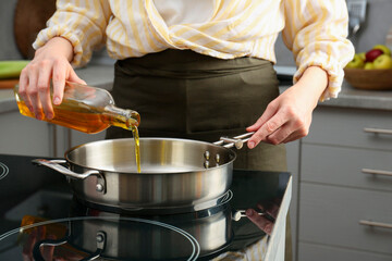 Vegetable fats. Woman pouring oil into frying pan on cooktop in kitchen, closeup