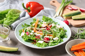 Bowl of fresh salad with feta cheese and different vegetables on grey background