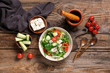 Bowl of fresh vegetable salad with cucumber and feta cheese on wooden background