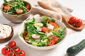 Bowls of fresh vegetable salad with cucumber and feta cheese on white background