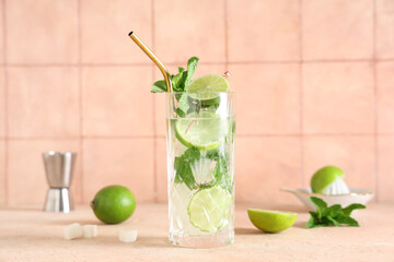 Glass of fresh Mojito cocktail with limes and mint on beige table