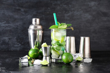 Glass of fresh Mojito cocktail with limes and shaker on black background
