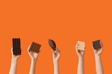 Female hands with different sweet chocolate and cocoa pod on orange background