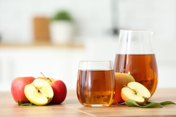 Glass and jug of fresh apple juice on wooden table in kitchen