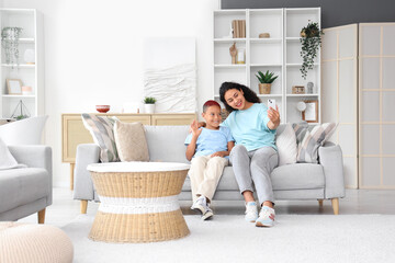 Little African-American boy with his mother taking selfie on sofa at home